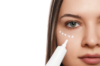Photo of Young woman applying cream under eye on white background, closeup