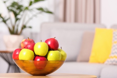 Photo of Bowl with different sweet apples on table in living room, space for text