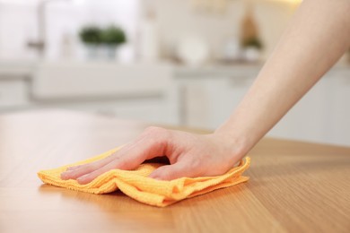 Woman with microfiber cloth cleaning wooden table in kitchen, closeup