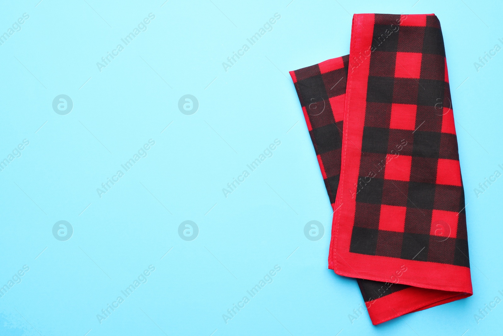 Photo of Folded red checkered bandana on light blue background, top view. Space for text