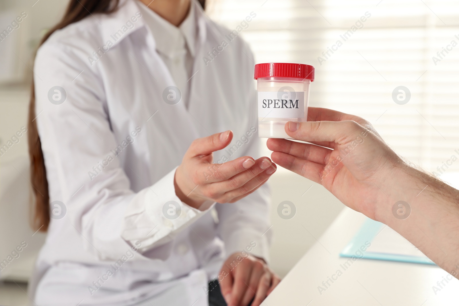 Photo of Donor giving container of sperm to doctor in hospital, closeup