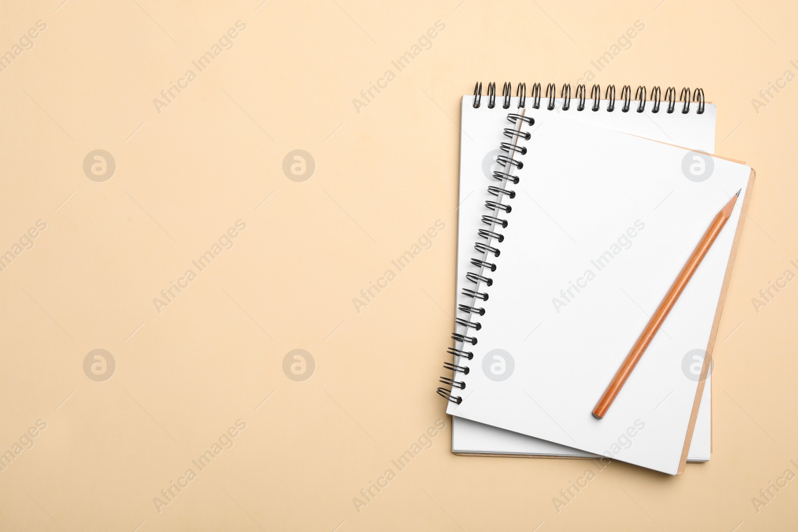 Photo of Open notebooks and pencil on beige background, top view. Space for text