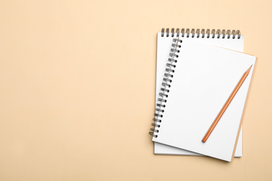 Photo of Open notebooks and pencil on beige background, top view. Space for text