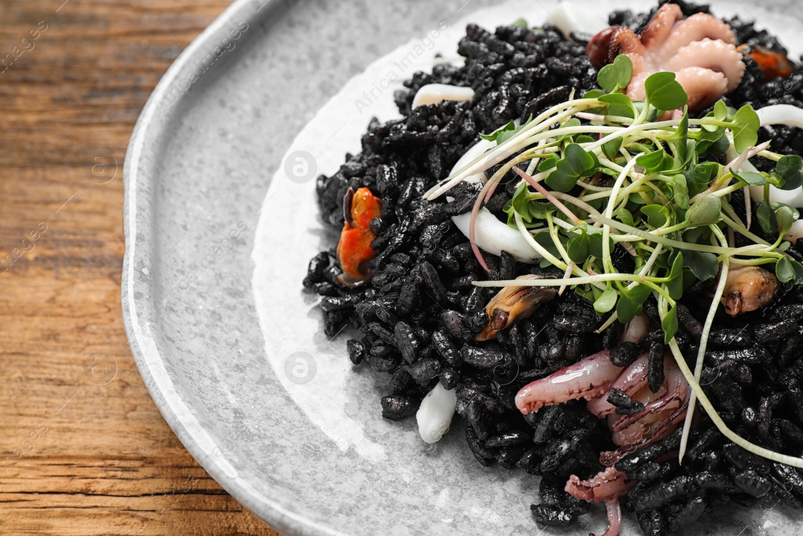 Photo of Delicious black risotto with seafood on wooden table, closeup