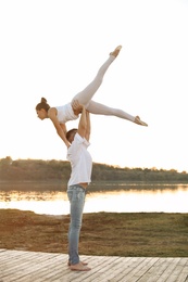 Beautiful young couple practicing dance moves near river at sunset