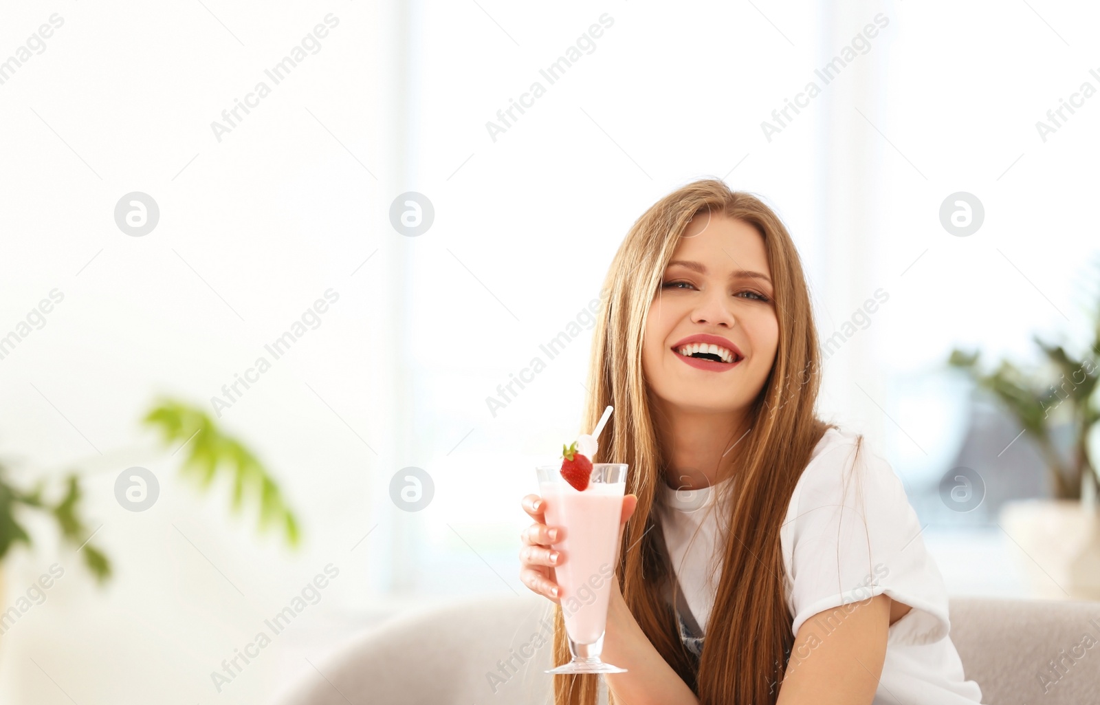 Photo of Young woman with glass of delicious milk shake indoors