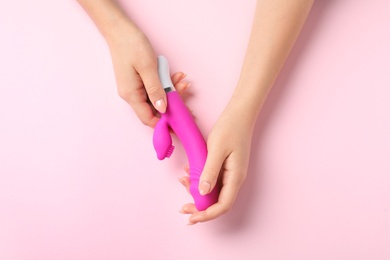 Young woman holding vibrator on pink background, top view. Sex toy