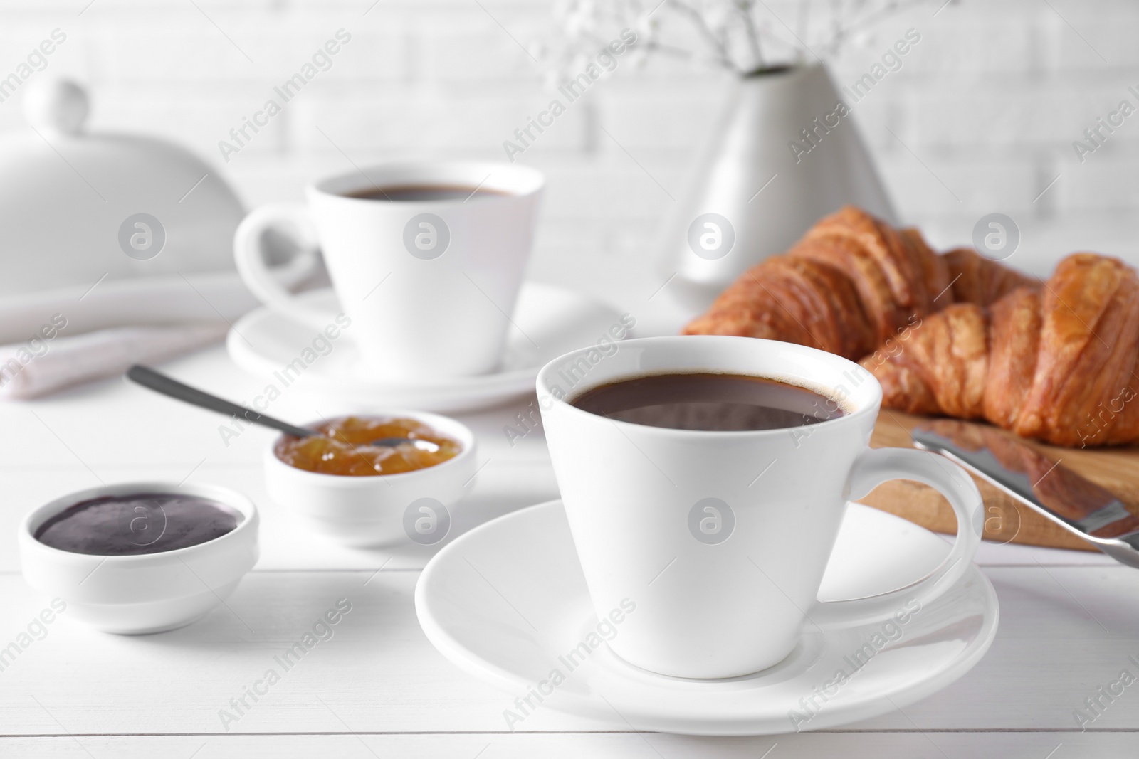 Photo of Cup of coffee, jam and croissants on white wooden table. Tasty breakfast