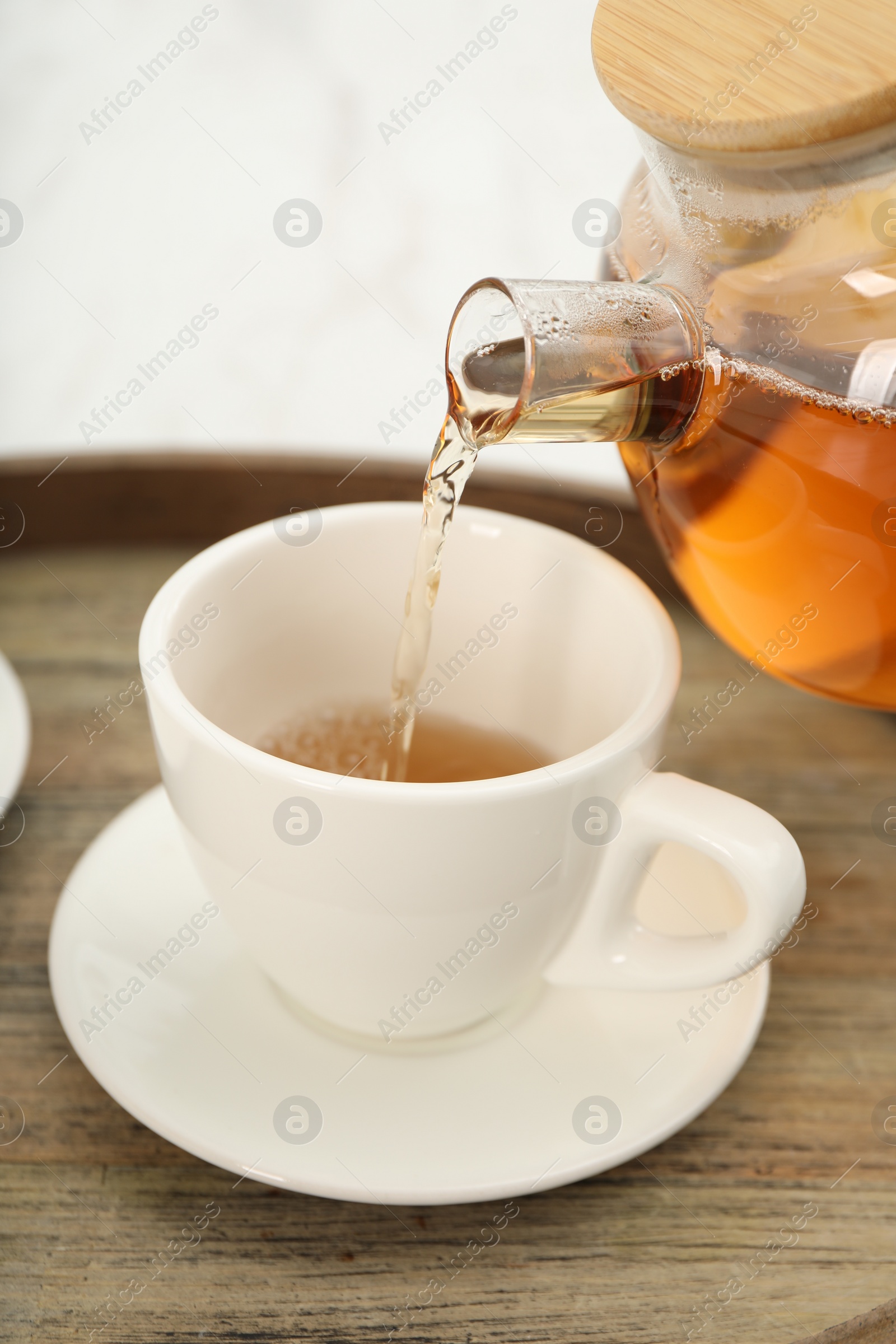 Photo of Pouring aromatic tea in cup at table, closeup