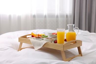 Photo of Wooden tray with tasty breakfast on bed at home