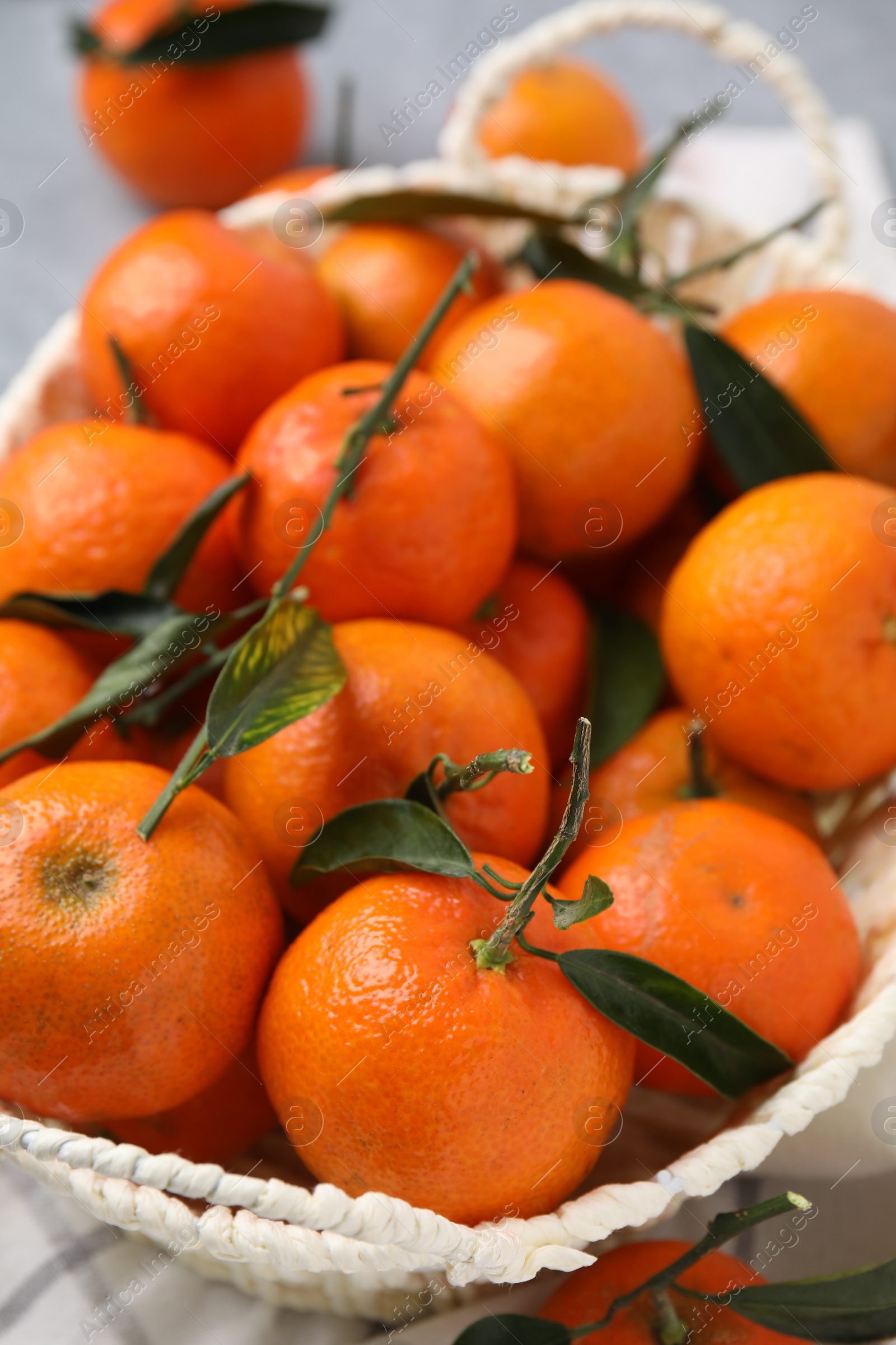 Photo of Fresh ripe tangerines and leaves in basket on table, closeup