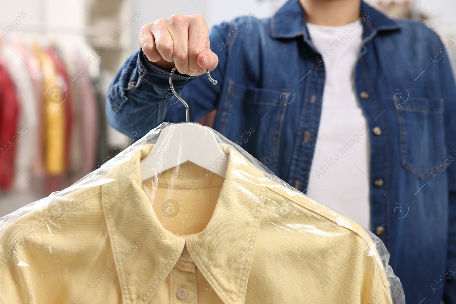 Photo of Dry-cleaning service. Woman holding shirt in plastic bag indoors, closeup