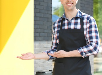 Photo of Young waiter in uniform near restaurant entrance outdoors
