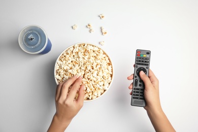 Photo of Woman with TV remote eating popcorn on white background, top view. Watching cinema