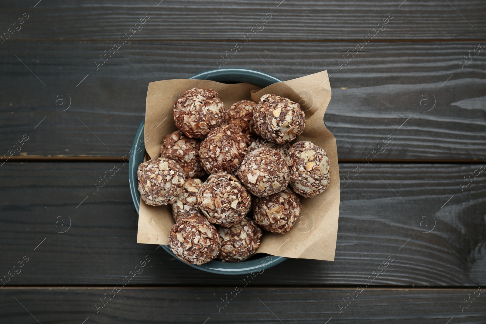 Photo of Bowl of delicious sweet chocolate candies on dark wooden table, top view