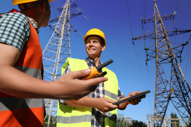 Professional electricians in uniforms near high voltage towers