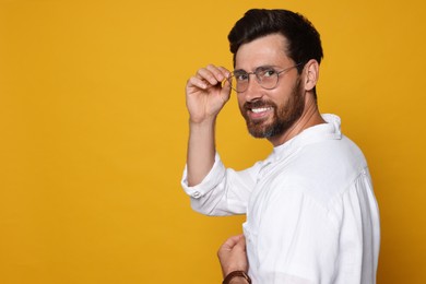 Photo of Portrait of smiling bearded man with glasses on orange background. Space for text