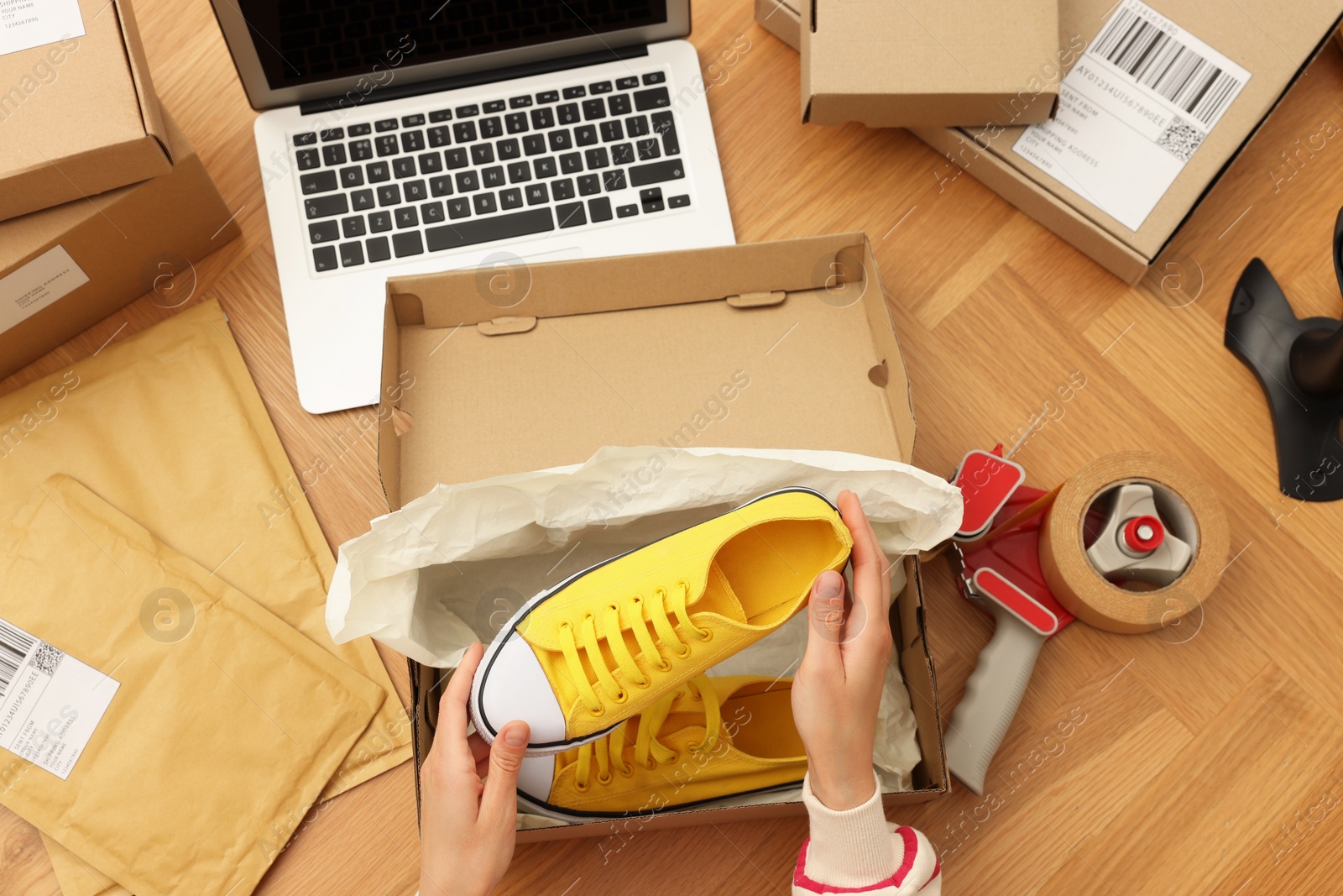 Photo of Woman packing sneakers into cardboard box at wooden table, top view. Online store