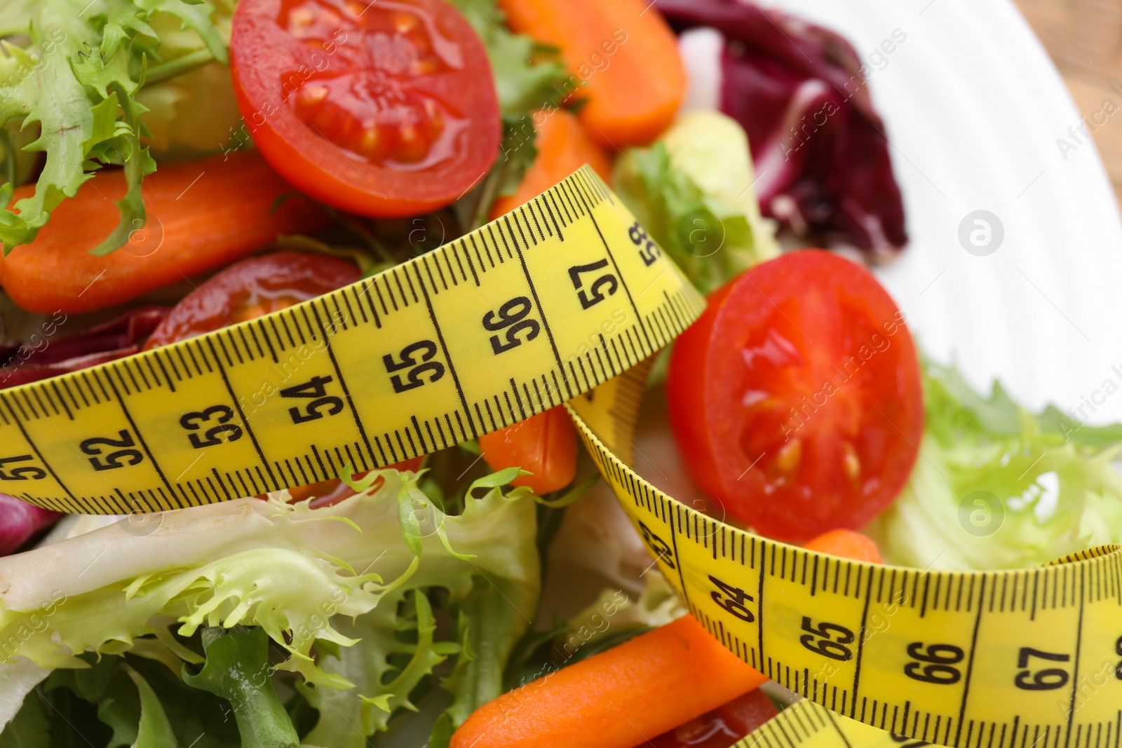 Photo of Plate with fresh vegetable salad and measuring tape, closeup. Healthy diet concept