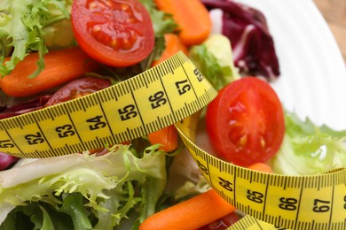 Photo of Plate with fresh vegetable salad and measuring tape, closeup. Healthy diet concept
