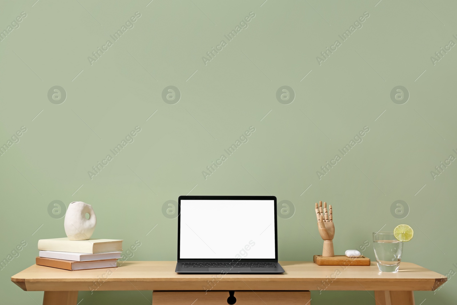 Photo of Stylish workplace with laptop, books and decor on table near light green wall