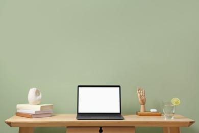 Photo of Stylish workplace with laptop, books and decor on table near light green wall