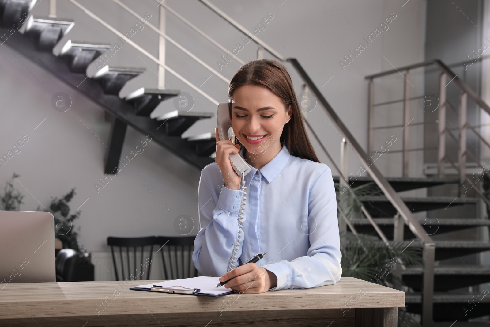 Photo of Female receptionist with clipboard talking on phone at workplace