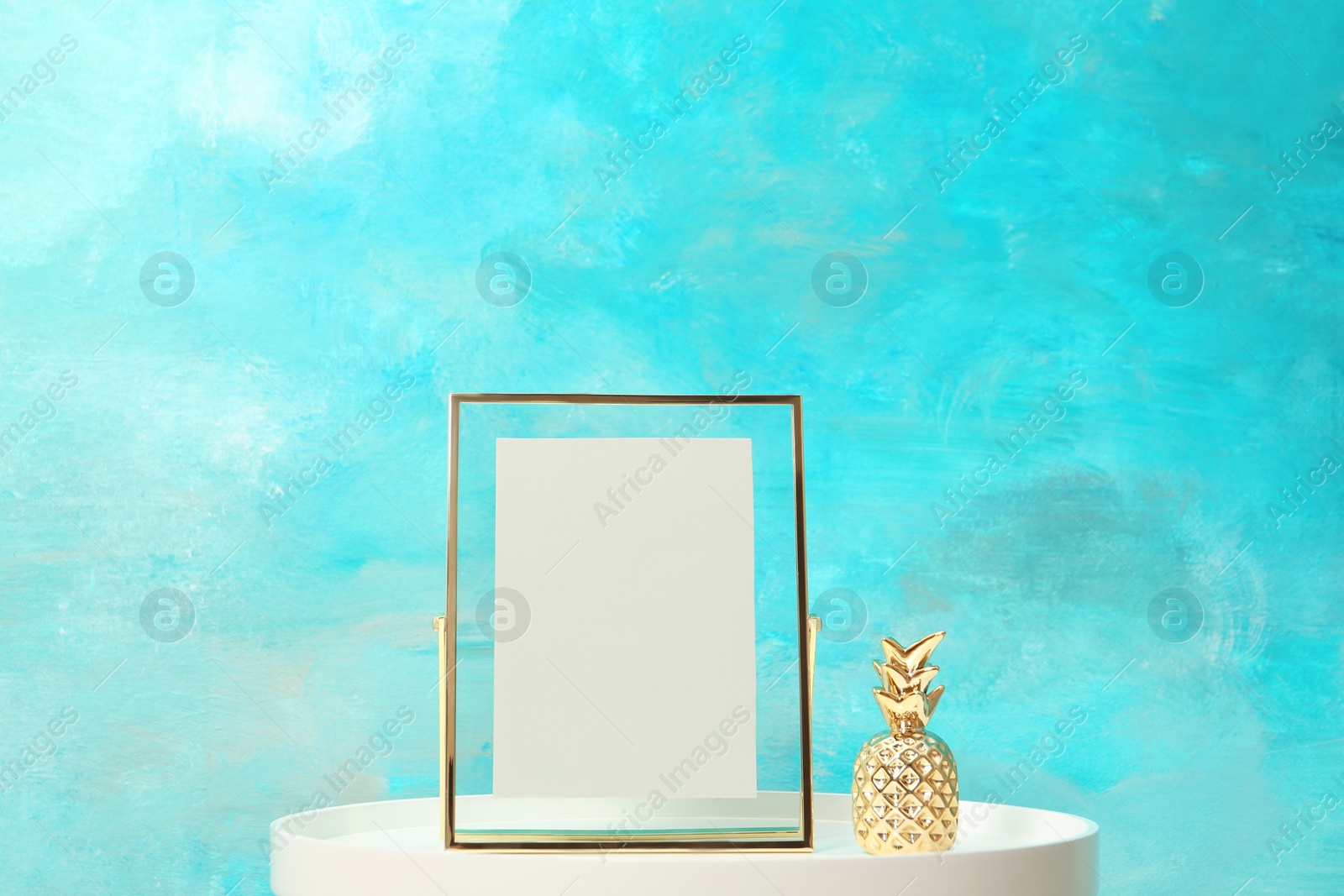 Photo of Blank frame and decorative pineapple figure on table near color wall. Mock up for design