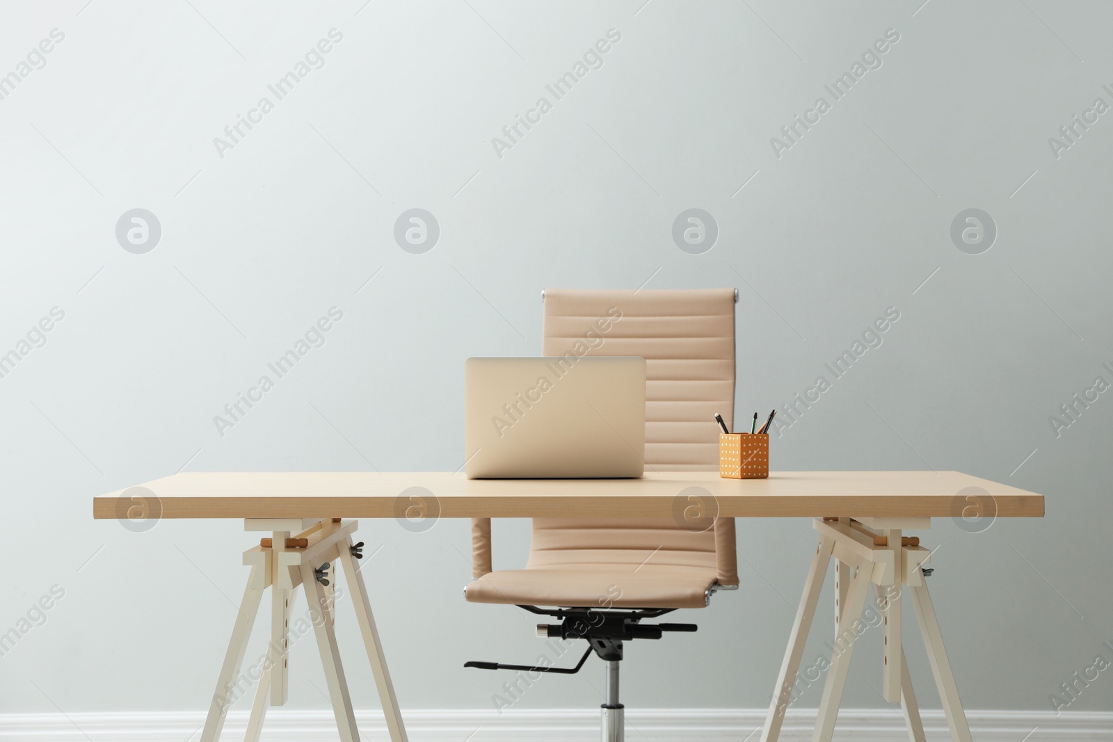 Photo of Stylish workplace with laptop and comfortable armchair near light wall indoors. Interior design