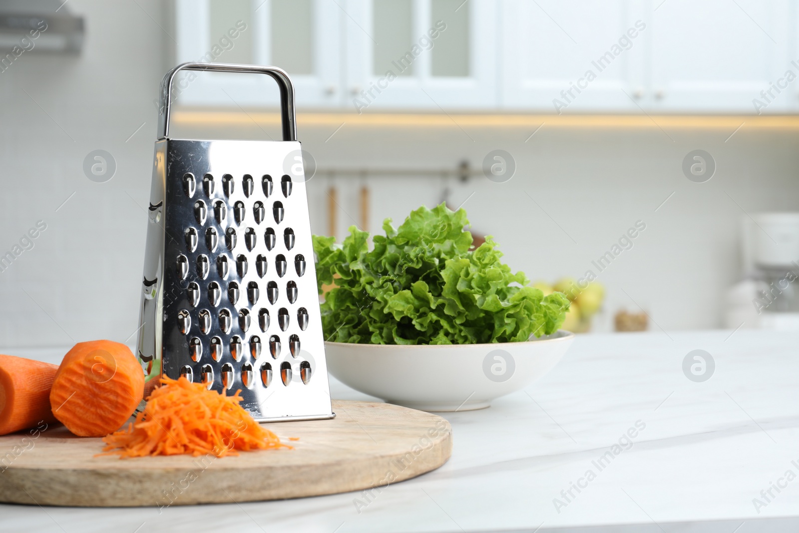 Photo of Grater and fresh ripe carrot on white table in kitchen. Space for text