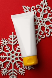 Photo of Tube of hand cream and snowflakes on red background, flat lay. Winter skin care