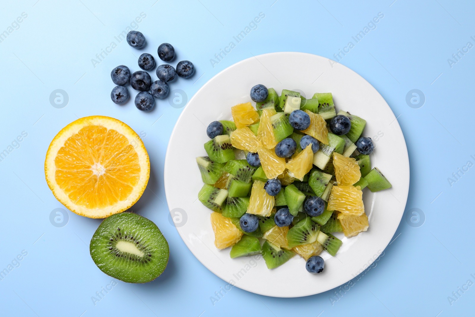 Photo of Plate of tasty fruit salad and ingredients on light blue background, flat lay