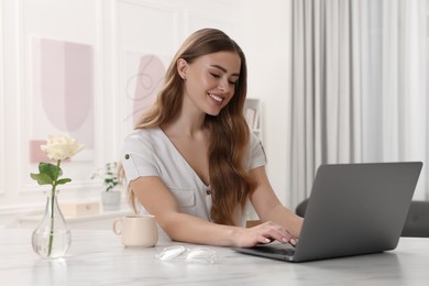 Happy woman using laptop at white table in room