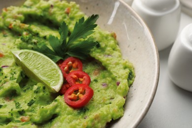 Bowl of delicious guacamole served with lime, pepper and parsley on table, closeup