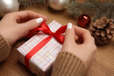 Woman wrapping Christmas gift at wooden table, closeup
