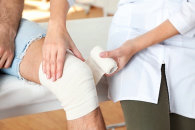 Photo of Doctor applying bandage to patient's knee in clinic, closeup