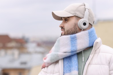 Photo of Handsome man in warm scarf and headphones on blurred background. Space for text