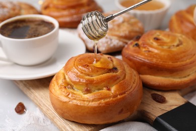Photo of Pouring honey onto delicious rolls with raisins at table, closeup. Sweet buns
