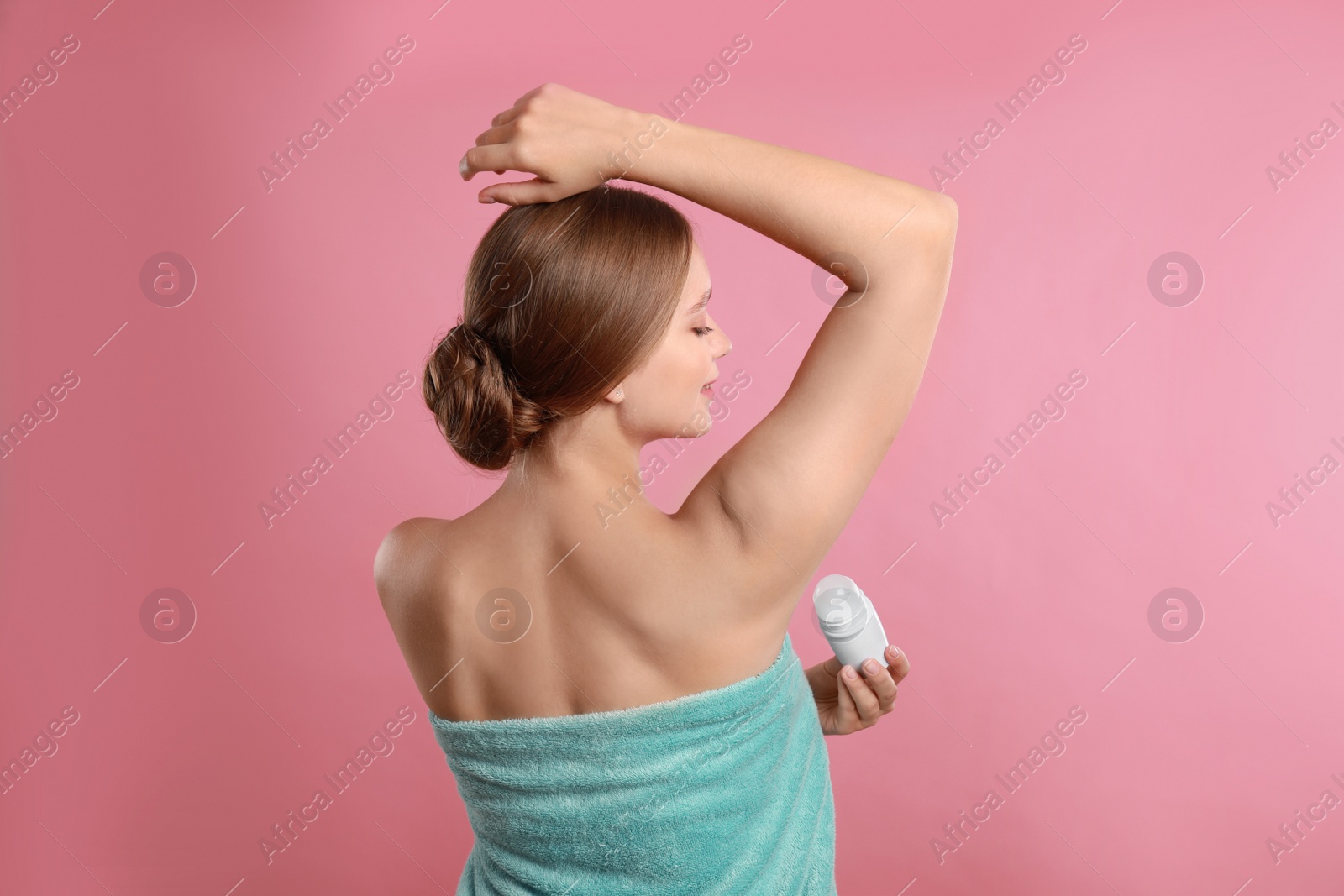 Photo of Young woman applying deodorant to armpit on pink background