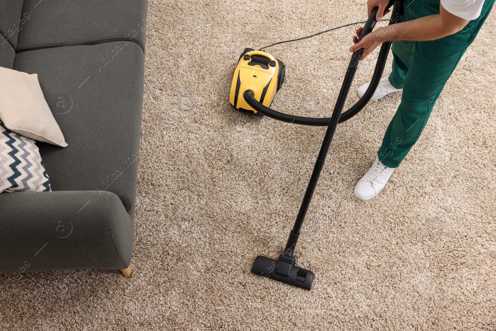 Photo of Dry cleaner's employee hoovering carpet with vacuum cleaner indoors, above view