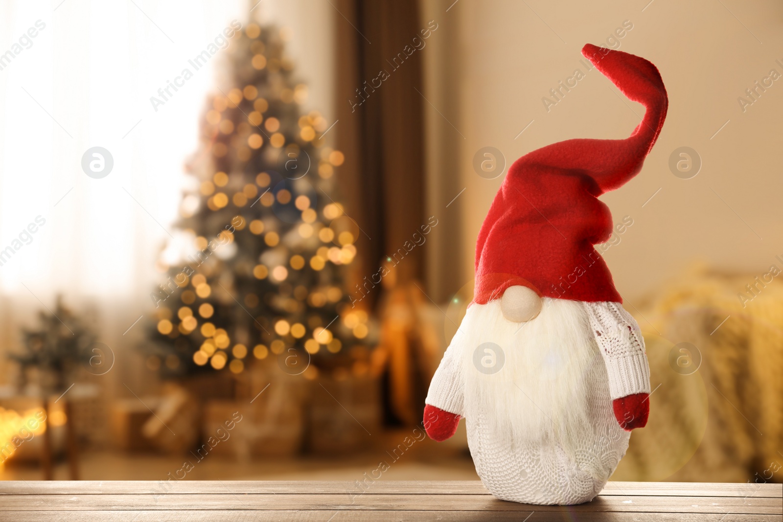 Image of Funny Christmas gnome on wooden table in room with festive decorations. Space for text