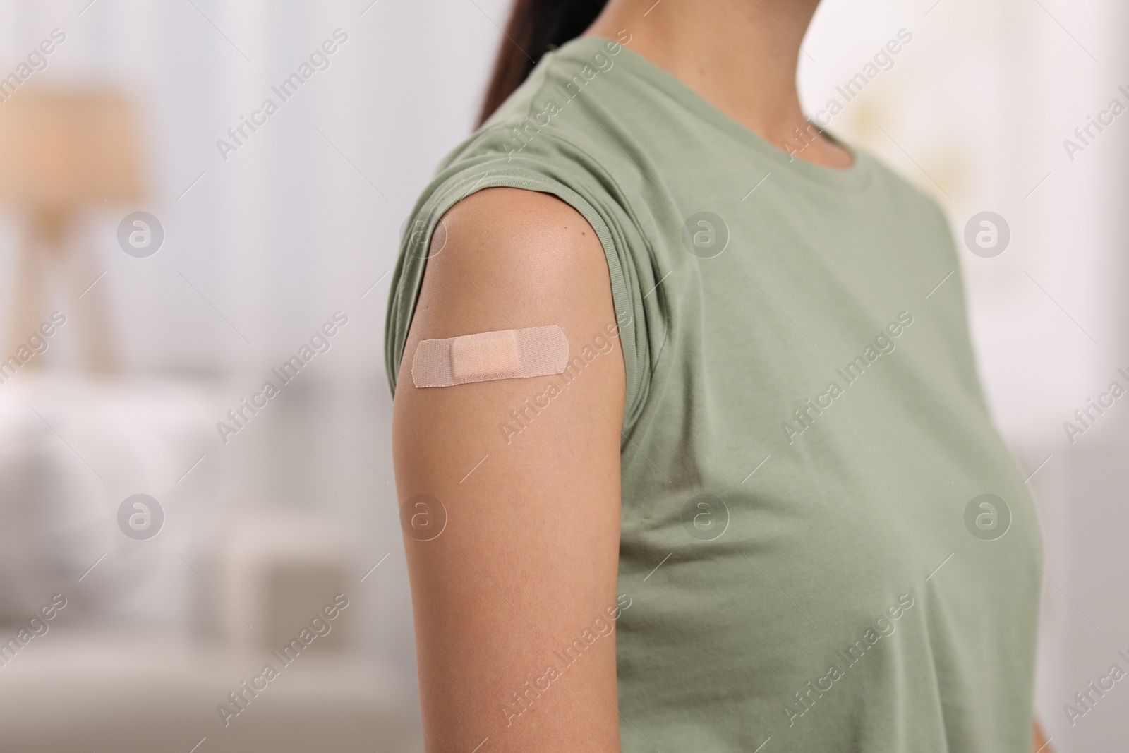 Photo of Woman with sticking plaster on arm after vaccination at home, closeup