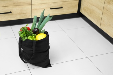 Photo of Tote bag with vegetables and fruit on floor in kitchen. Space for text