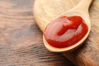 Spoon of tasty ketchup on wooden table, closeup. Space for text