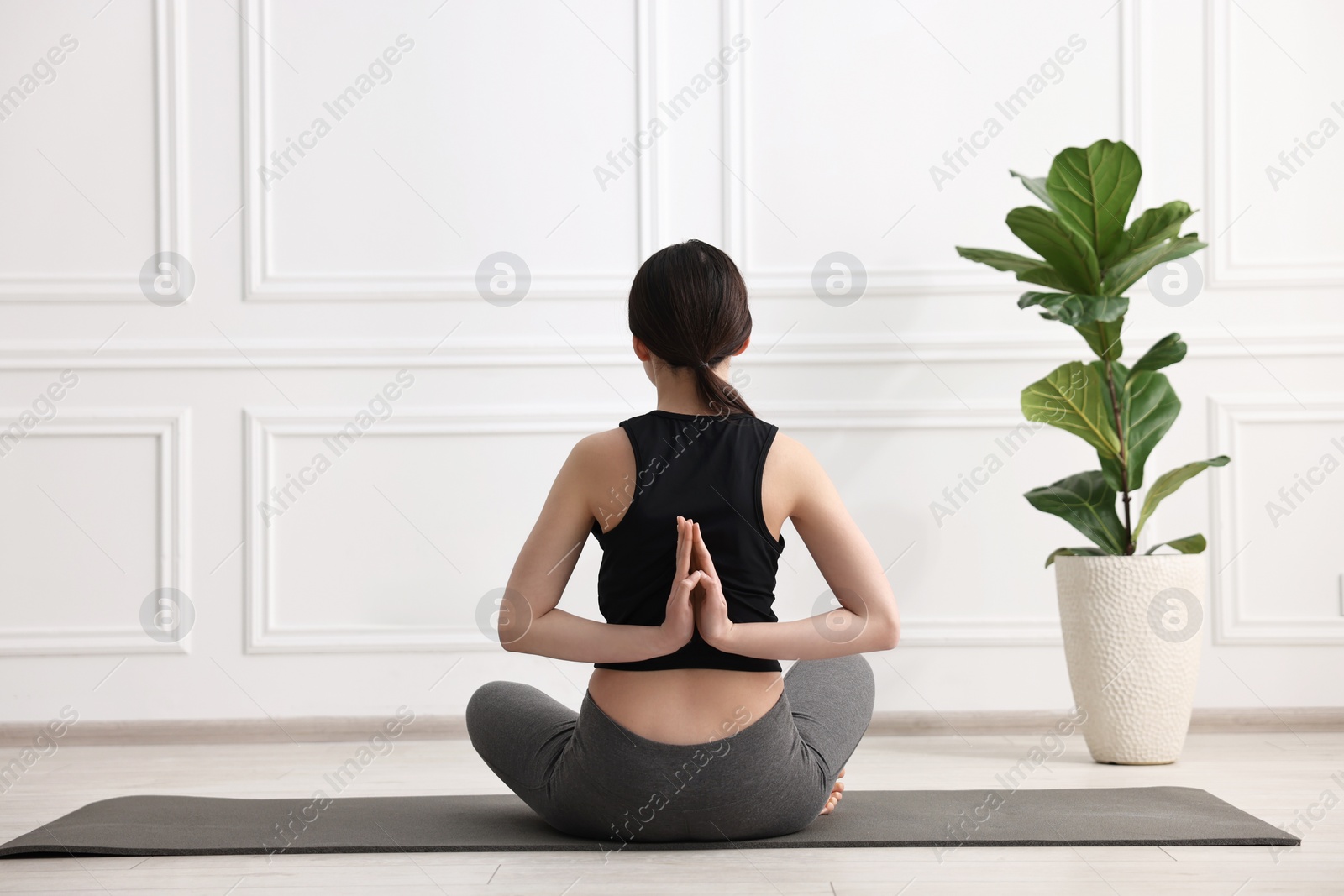 Photo of Girl practicing vajrasana with namaste behind back on mat in yoga studio