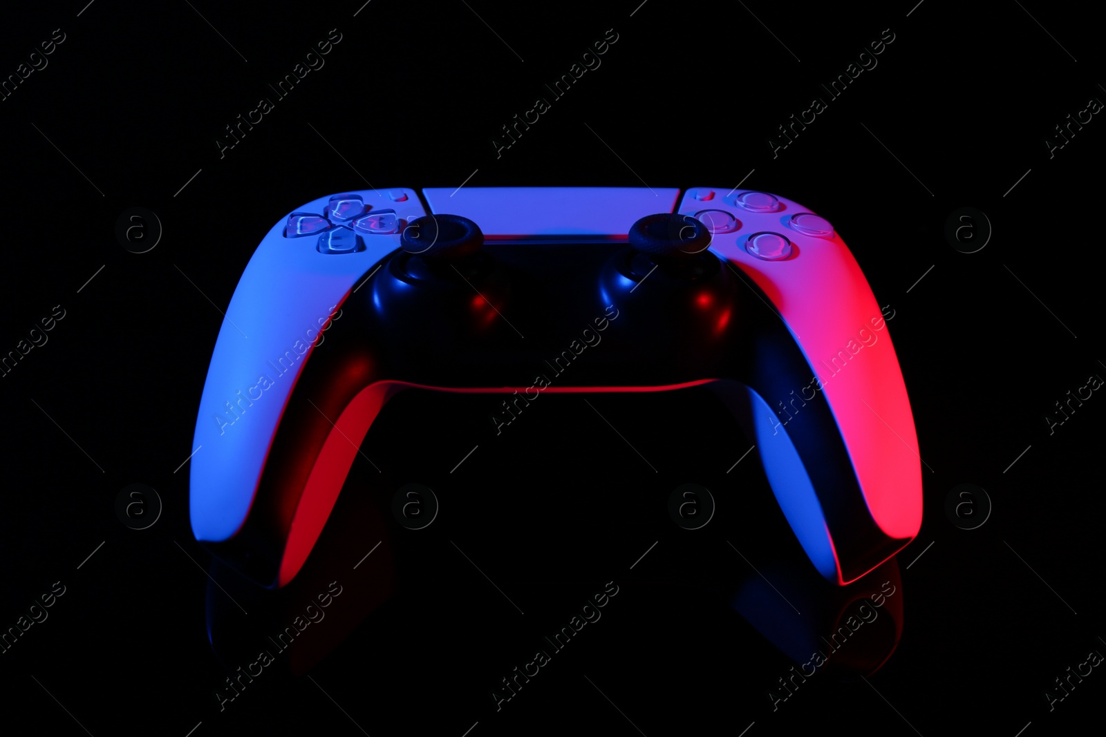 Photo of Wireless game controller on black mirror surface in neon lights