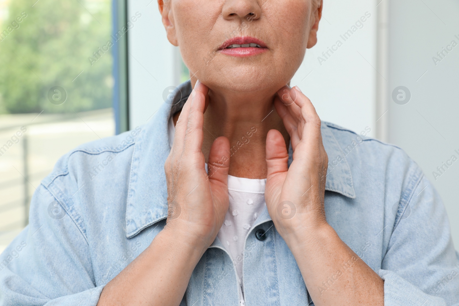 Photo of Mature woman doing thyroid self examination near window, closeup