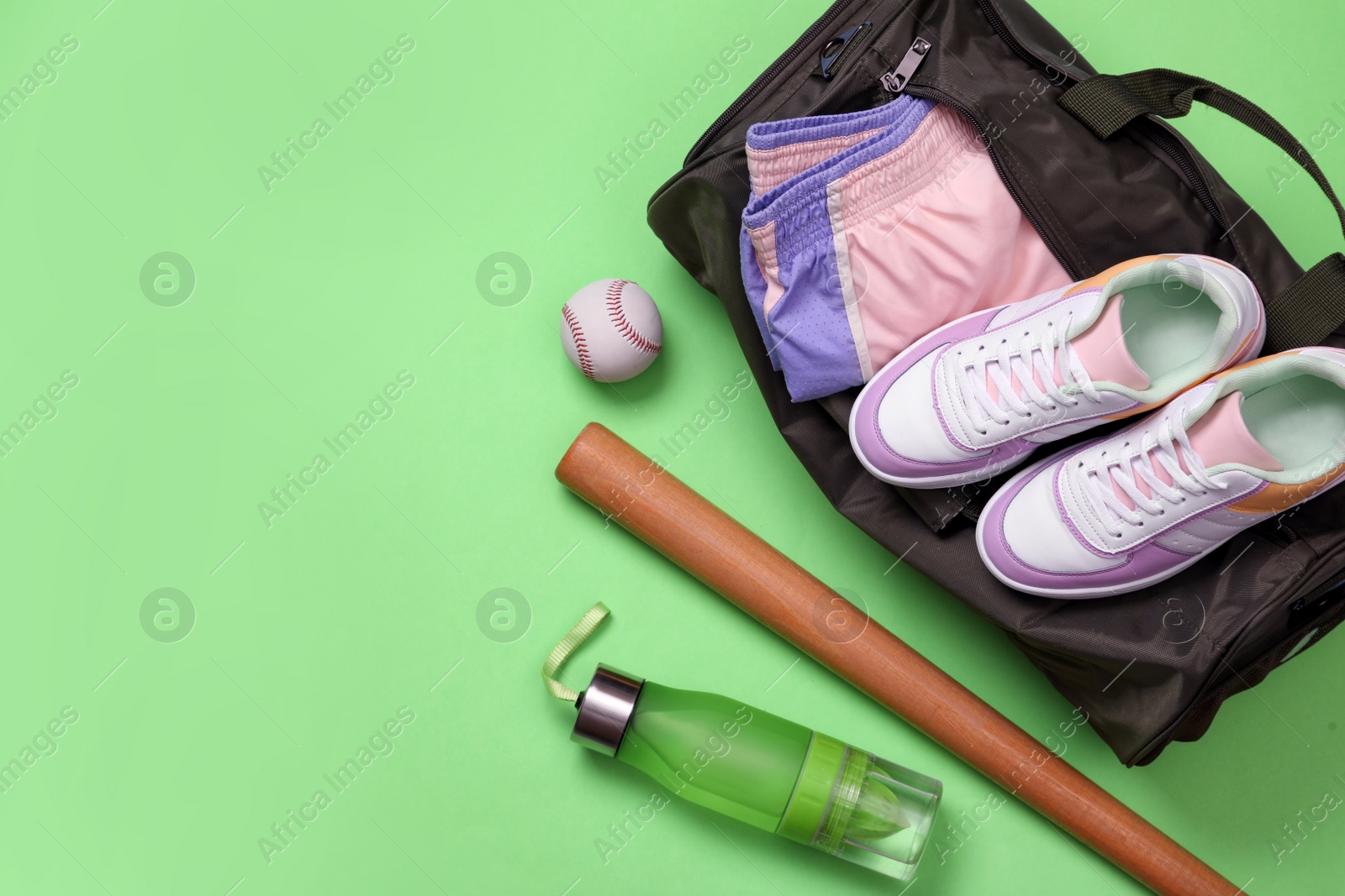 Photo of Sports bag and baseball equipment on light green background, flat lay. Space for text