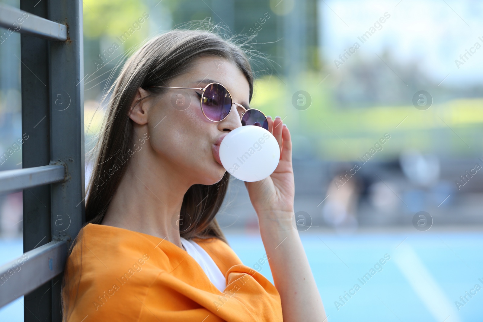 Photo of Beautiful young woman in sunglasses blowing bubble gum outdoors. Space for text