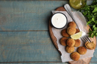 Photo of Delicious falafel balls with lime and sauce on light blue wooden table, flat lay. Space for text